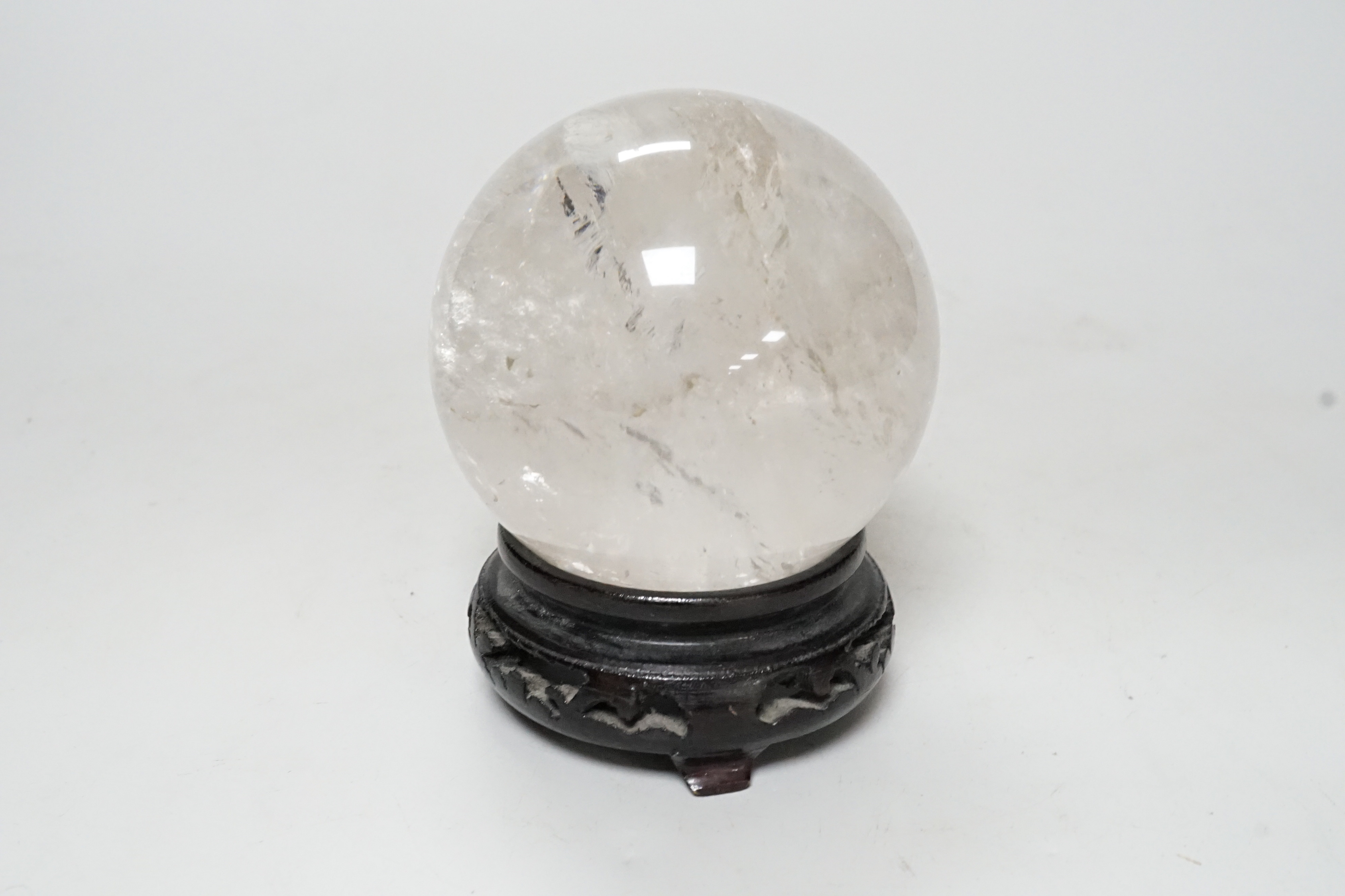 A rock crystal quartz sphere, probably from Brazil, on a carved wood stand, 10cm tall